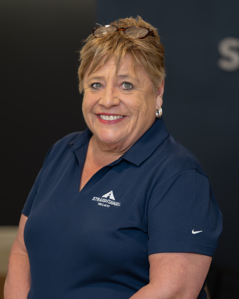 Smiling woman in a blue polo shirt standing in front of a dark background.