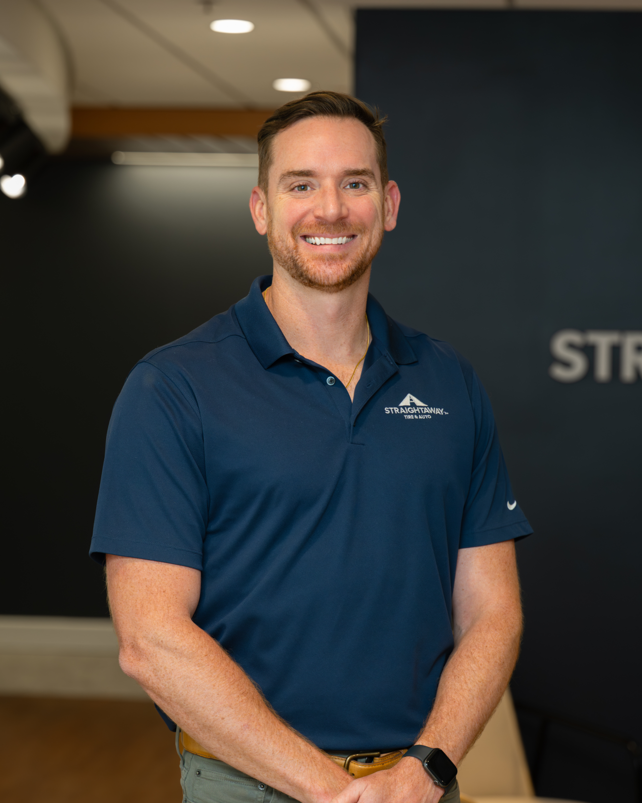 Smiling man in a blue polo shirt standing in an office setting, firm logo visible on his shirt.