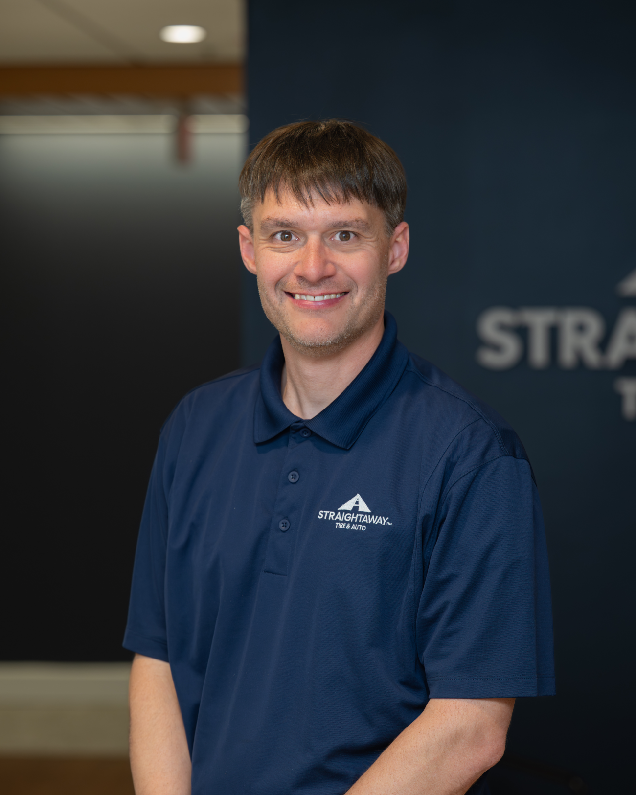 Man in a blue Straightaway Tire & Auto polo shirt smiling in an office setting.
