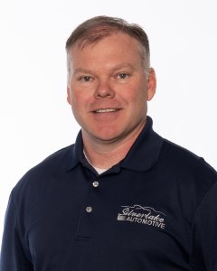 Man In A Blue Polo Shirt With Silverlake Automotive Logo, Poses Against A White Background, Smiling Slightly.