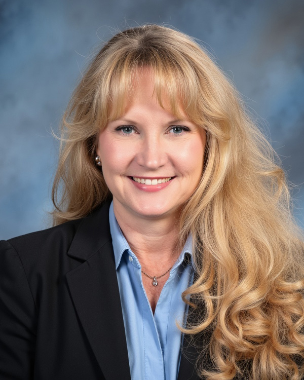 Smiling woman with long blonde hair in a business suit against a blue background. Professional headshot.