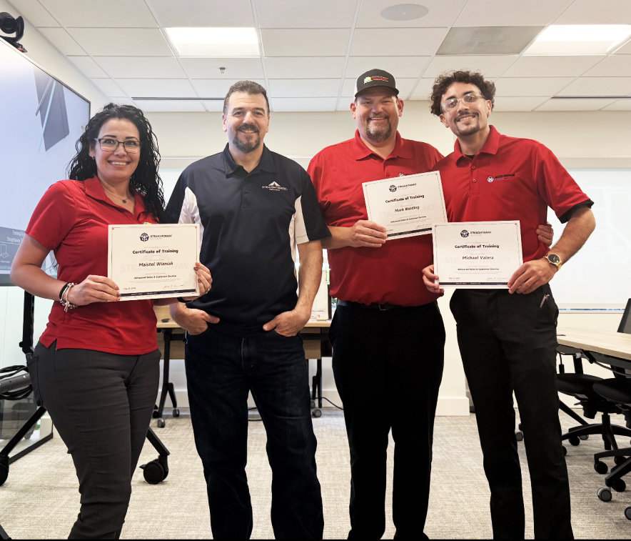 Four people smiling and holding certificates in an office setting.