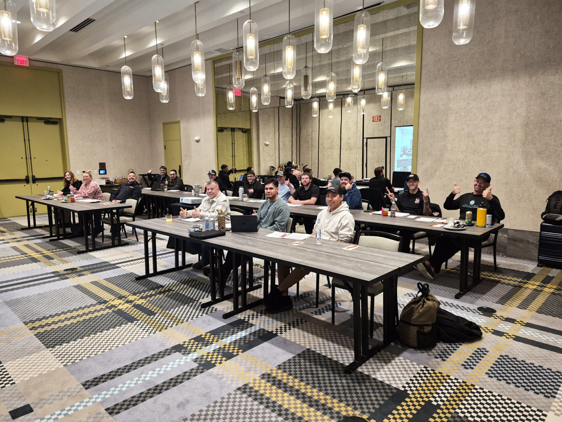 People in a conference room attending a workshop, seated at long tables with laptops and notes.