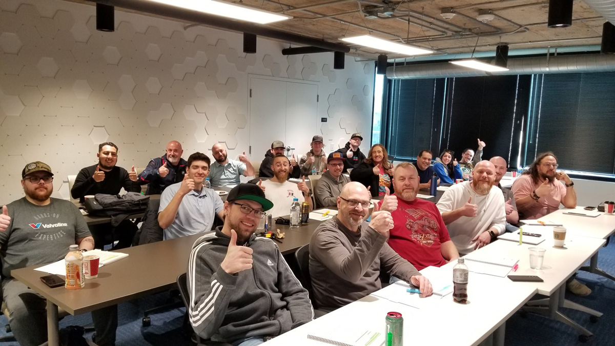 Group of people in a classroom giving thumbs up, showing enthusiasm and teamwork in a workshop setting.