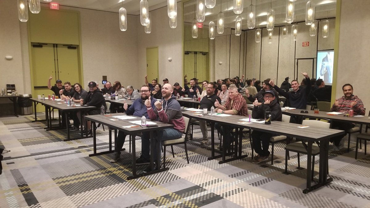 Indoor training session with engaged audience giving thumbs up, sitting at tables in a modern conference room.