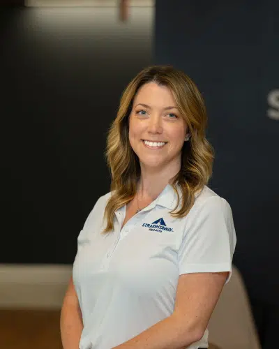 Smiling woman in branded shirt poses in professional setting with dark background.