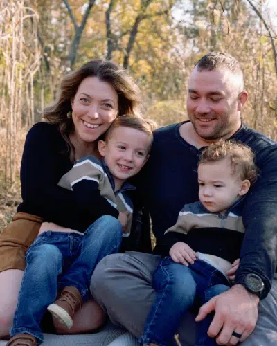 Happy family sitting outdoors in autumn, parents with two young children, smiling and enjoying nature.