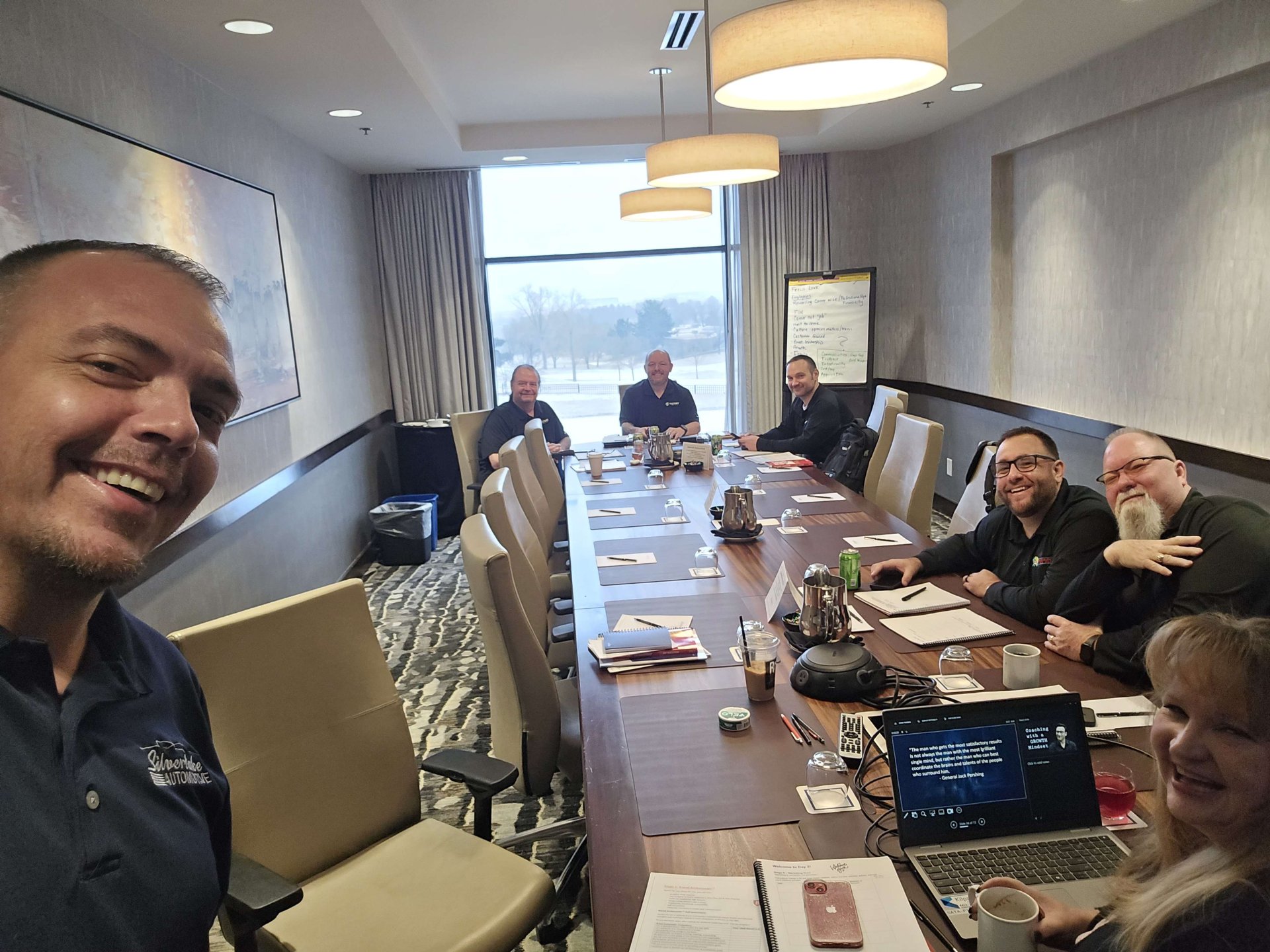 Team members in a boardroom having a meeting with laptops and notes, smiling for a group photo.