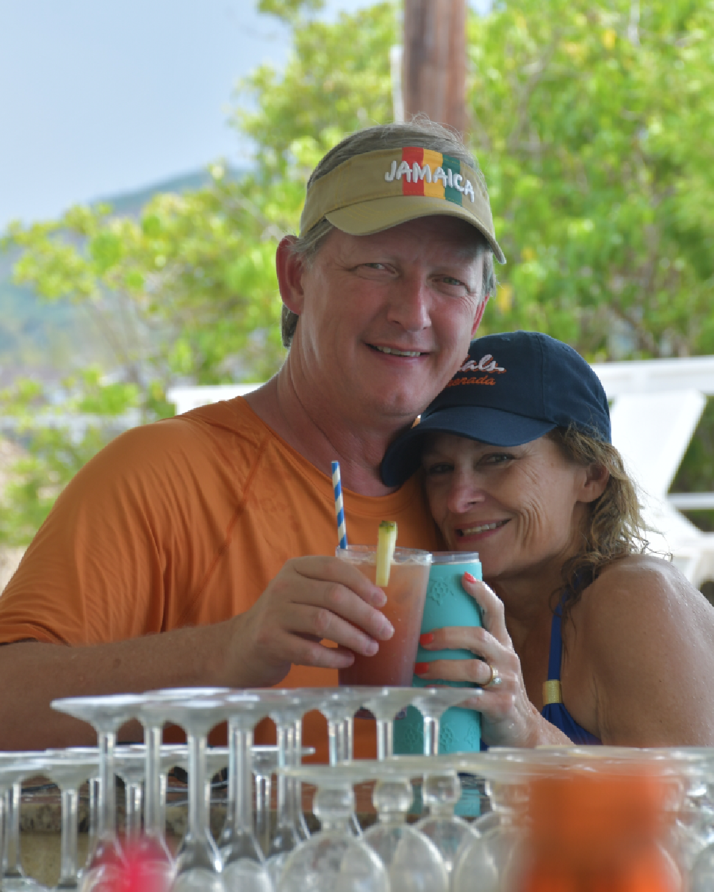 Couple enjoying tropical drinks at a bar with lush greenery in the background.